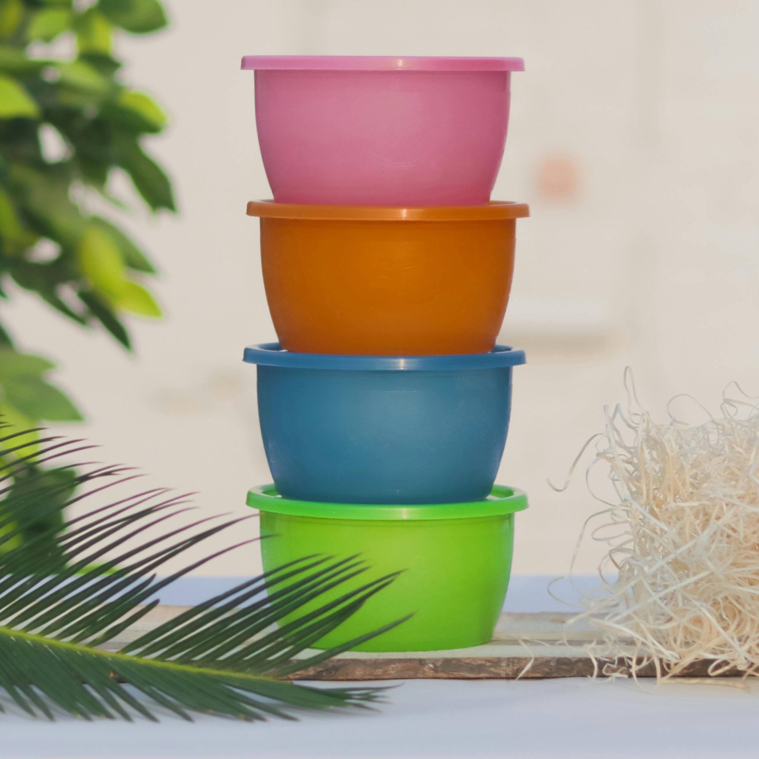 Vibrant plastic containers stacked outdoors with natural decor and foliage.