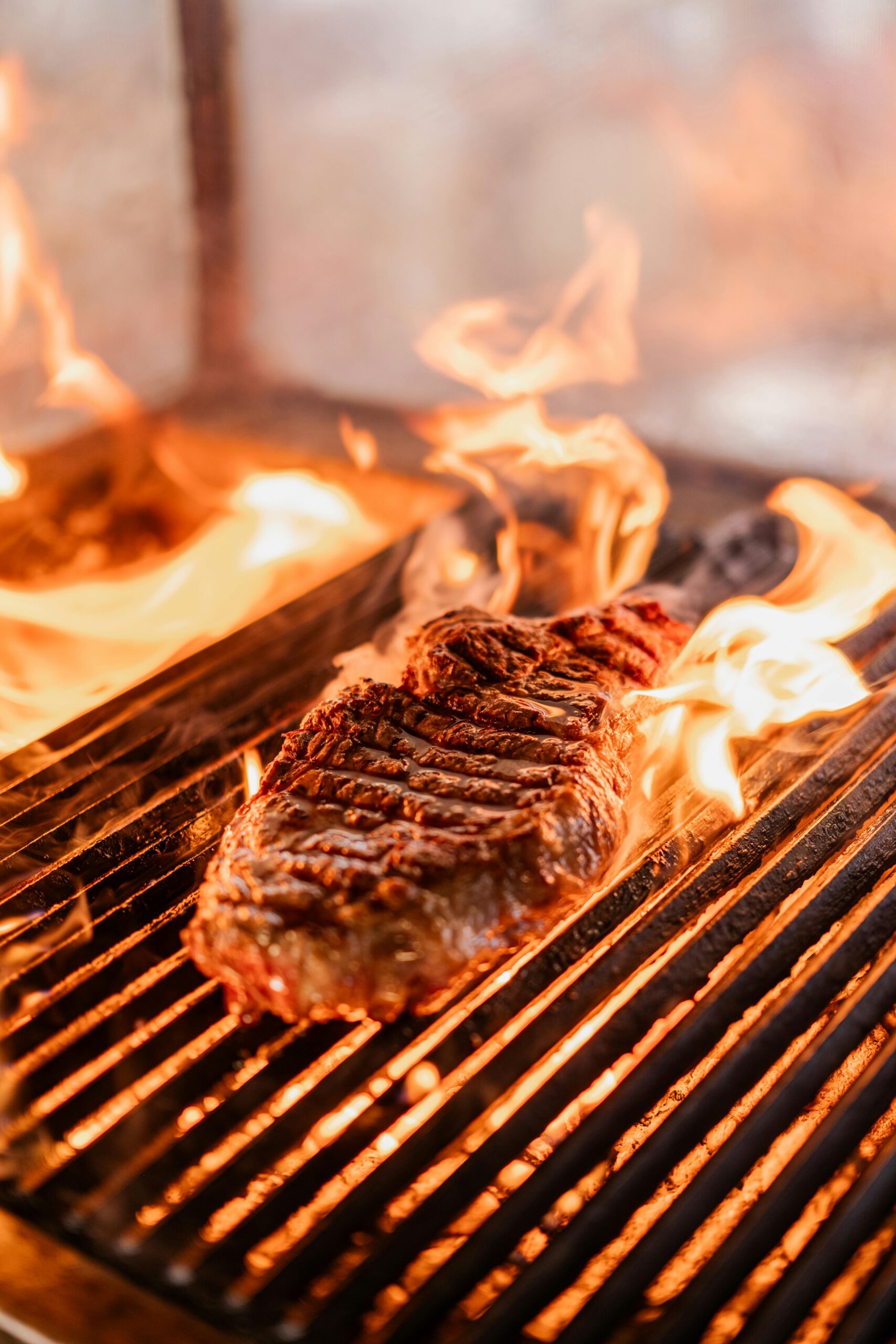 Close-up of a juicy steak sizzling on a hot grill surrounded by dancing flames.