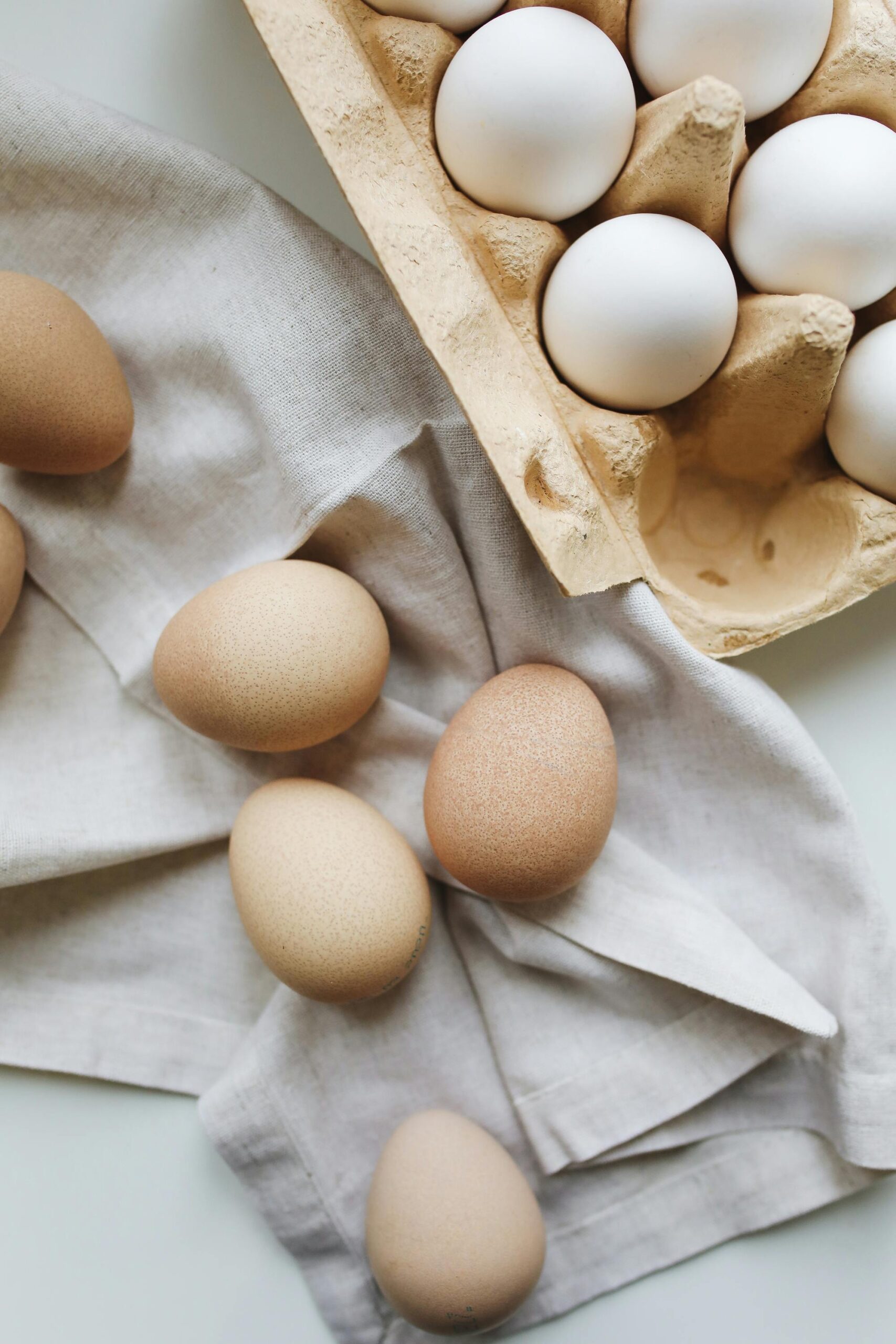 Brown and white eggs arranged creatively on textured fabric and egg carton, showcasing their natural beauty.