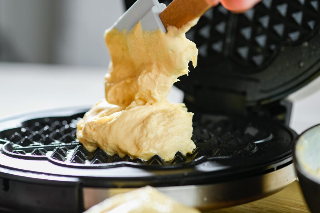 Delicious waffle batter being spread on a waffle maker for a tasty breakfast.
